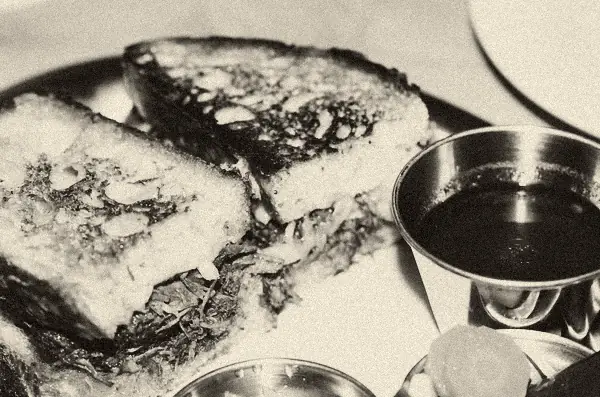 Ein getoastetes Sandwich mit geschmortem Fleisch, daneben ein Schälchen Brühe zum Tunken.
