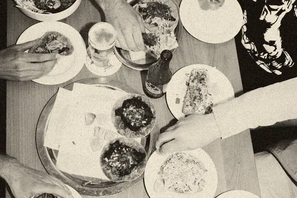 Ein Tisch von oben voller Tacos und Teller, mehrere Hände greifen gleichzeitig zu.