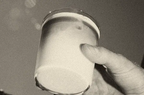 Eine Hand hält einen Eiskaffee mit Milch gegen den Himmel.